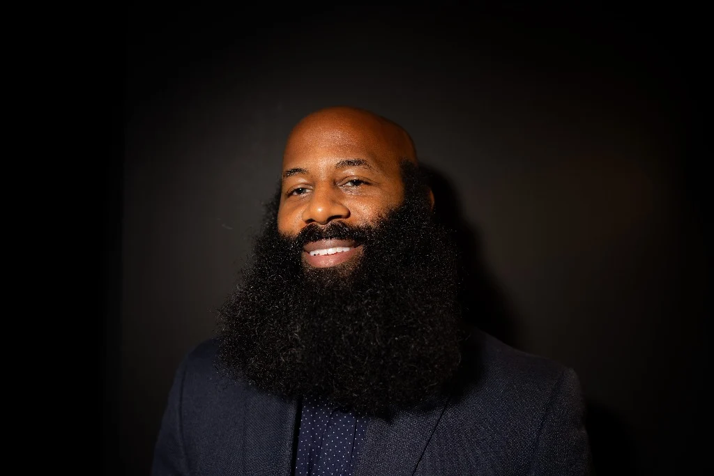 Anson smiling warmly in the studio, showcasing a well-maintained full beard.